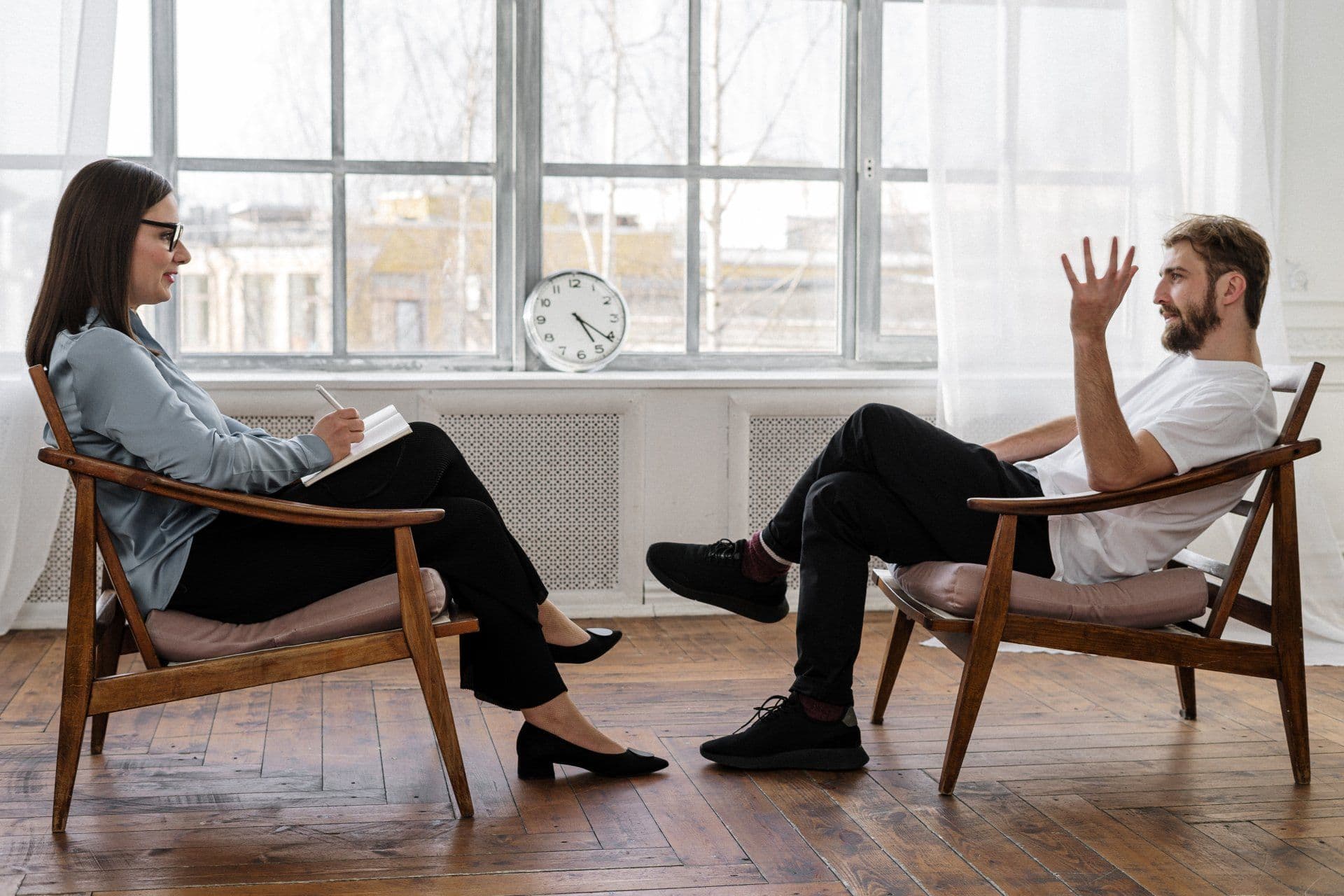 A man sitting in a chair talking to a woman who is taking notes depicting an advisory relationship.